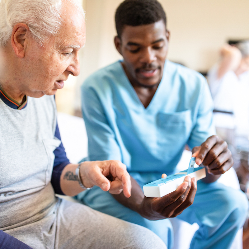A nurse dressed in blue helping patient with medications.